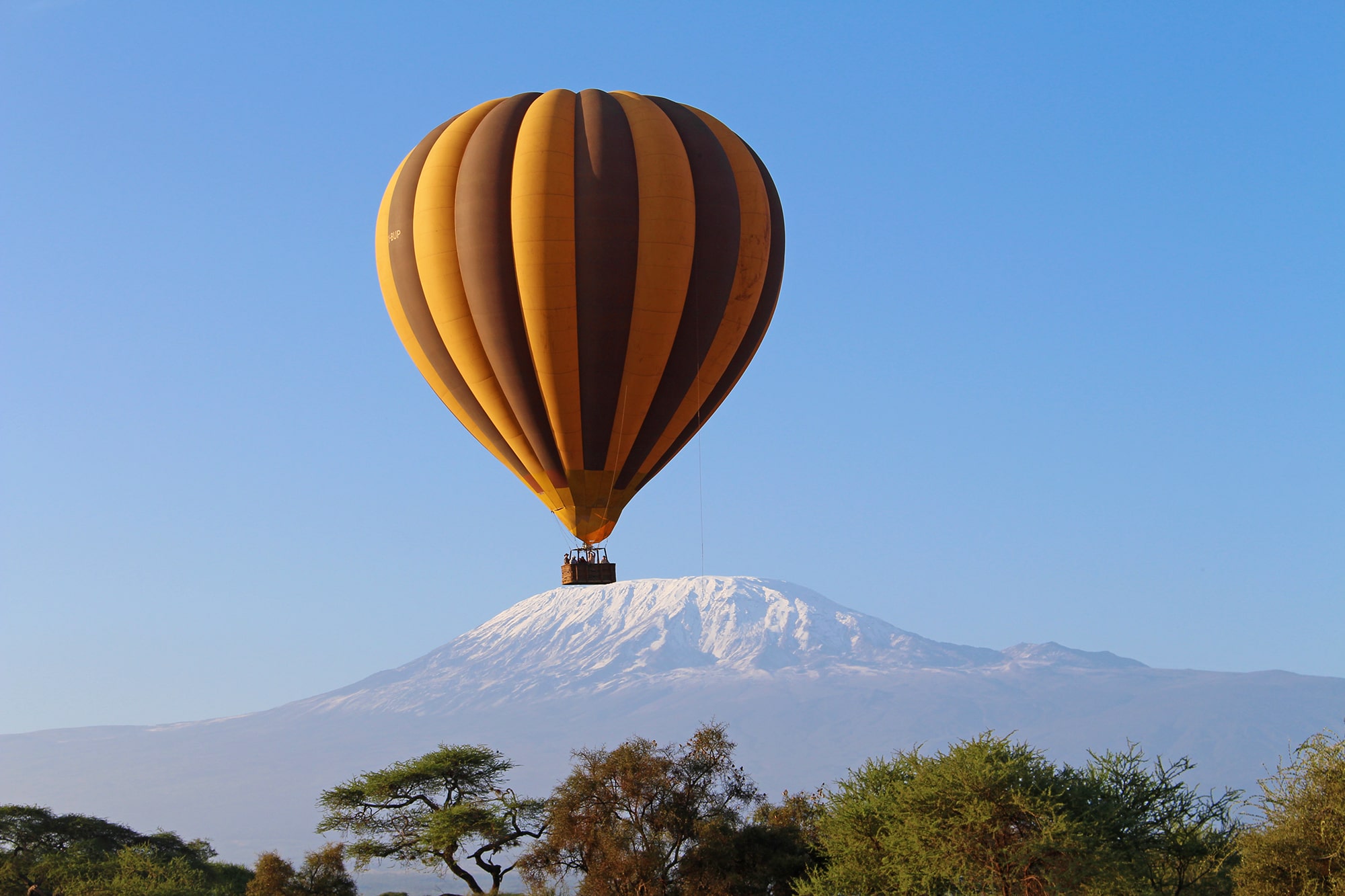 Image of a Kilimanjaro Balloon Safari hot air balloon floating in the air right in front of a clear view of Mount Kilimanjaro