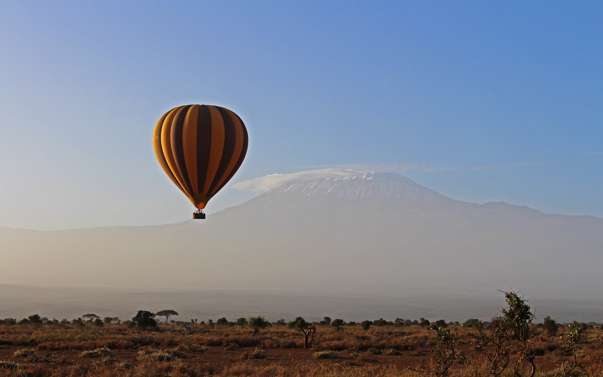Image of a Kilimanjaro Balloon Safari hot air balloon flying over the Amboseli landscape with Mount Kilimanjaro in the background on a clear sunny day